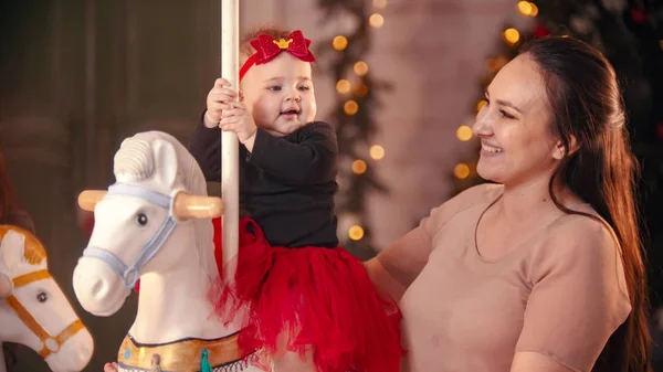 Χριστουγεννιάτικη ιδέα - μια χαμογελαστή γυναίκα με το μωρό της στο καρουζέλ — Φωτογραφία Αρχείου