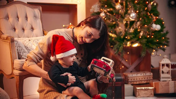 Una joven sonriente jugando con su pequeño bebé con un coche de juguete en el estudio de Navidad — Foto de Stock