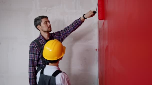 A man painting walls and gives his son the roller — Stock Video