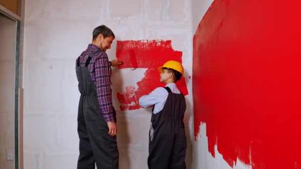 Ремонт квартиры - семья отца и сына, покрывающая стену красной краской — стоковое видео