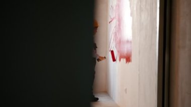 Daire onarılıyor. Kırmızı boyayla duvara çizgi çizen yorgun küçük çocuk.