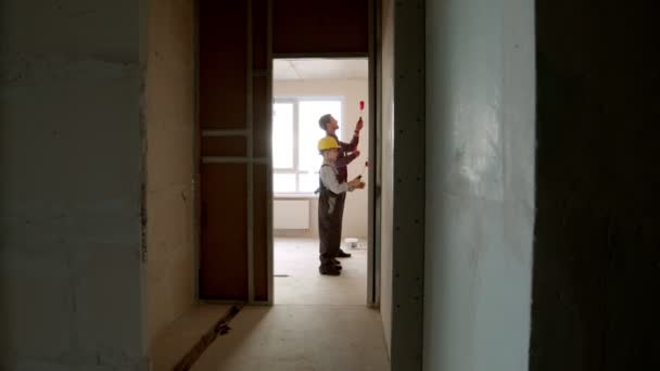 Remont mieszkania w dzień - mały chłopiec i jego ojciec malują ściany wewnątrz pokoju — Wideo stockowe