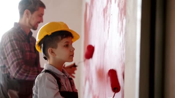 Ένα αγοράκι και ο πατέρας του βάφουν τοίχους με κόκκινο χρώμα στο νέο διαμέρισμα. — Αρχείο Βίντεο