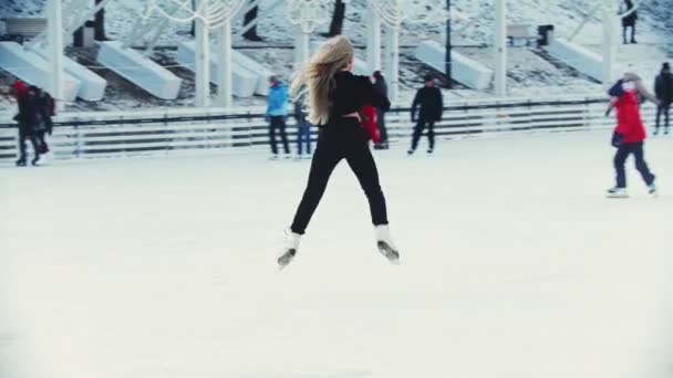Una joven rubia patinadora profesional realizando trucos en pista de hielo — Vídeos de Stock
