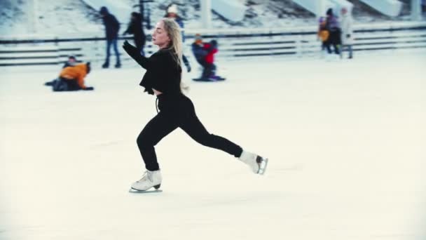 Uma jovem mulher loira profissional patinadora artística na pista de gelo ao ar livre — Vídeo de Stock