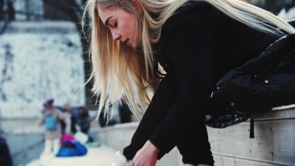 Uma jovem loira amarra seus patins antes de sair na pista — Vídeo de Stock