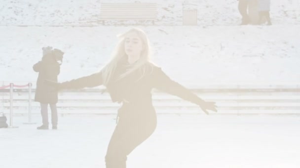 Uma jovem loira patinando na pista de gelo sob luz solar brilhante — Vídeo de Stock