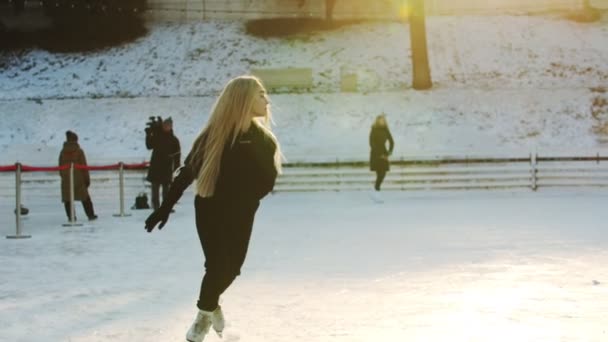 A young blonde woman skating on the ice rink outdoors — 비디오