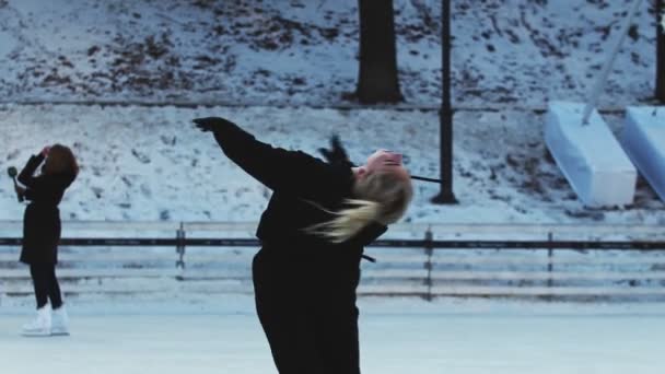 A young blonde woman figure skater spinning around herself on ice rink outdoors — Stock Video