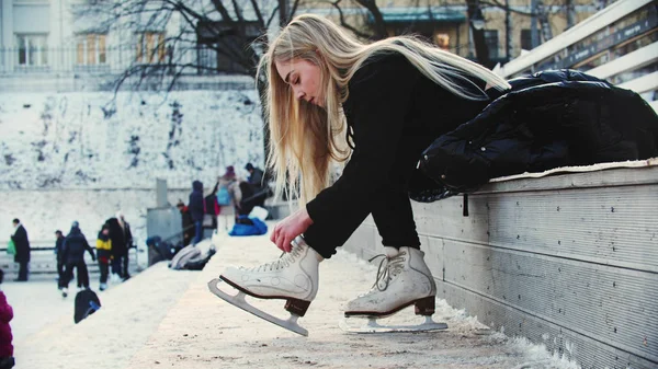 Uma jovem com cabelo loiro amarra seus patins antes de sair na pista — Fotografia de Stock