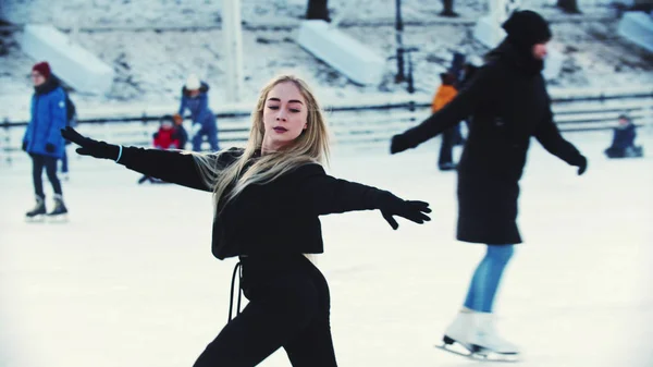 Een jonge blonde aantrekkelijke vrouw professionele kunstschaatser schaatsen op de buitenlucht ijsbaan rond mensen — Stockfoto