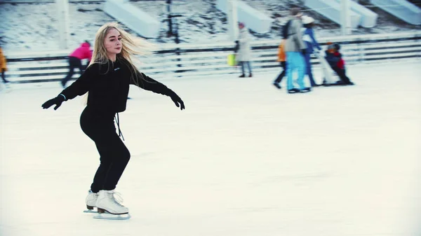 Eine junge Eiskunstläuferin läuft auf der Eisbahn um Menschen herum — Stockfoto