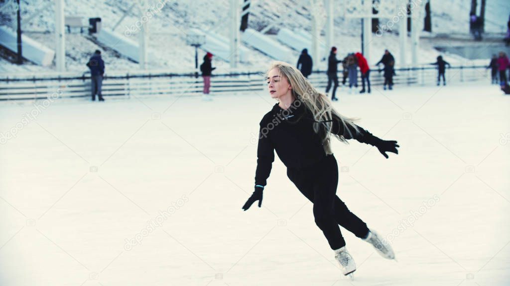 A young blonde attractive woman professional figure skater skating on the ice rink around people