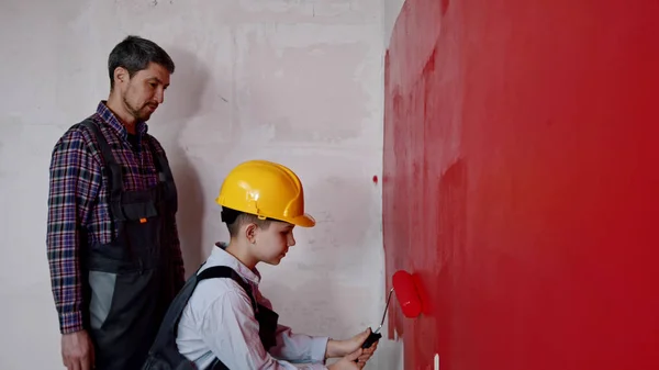 A little boy with father painting walls in red color in clear apartment