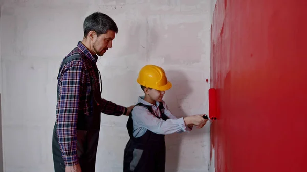 Ανακαίνιση διαμερίσματος - πατέρας και γιος που καλύπτουν τον τοίχο σε κόκκινο χρώμα στο νέο διαμέρισμα — Φωτογραφία Αρχείου