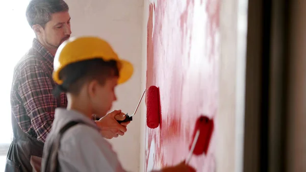 A little boy and his father painting walls in red color - a boy wearing helmet