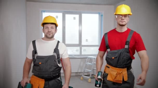 Dos trabajadores de pie en el apartamento de tiro sosteniendo sus instrumentos — Vídeo de stock