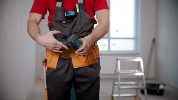 A young man worker takes out a big instrument from his tool belt — Stock Video