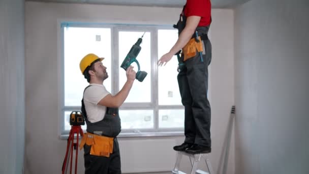 Wohnungsreparatur in Zugluftraum - ein Arbeiter reicht Bohrer an den anderen weiter - beginnt mit dem Bohren der Decke — Stockvideo