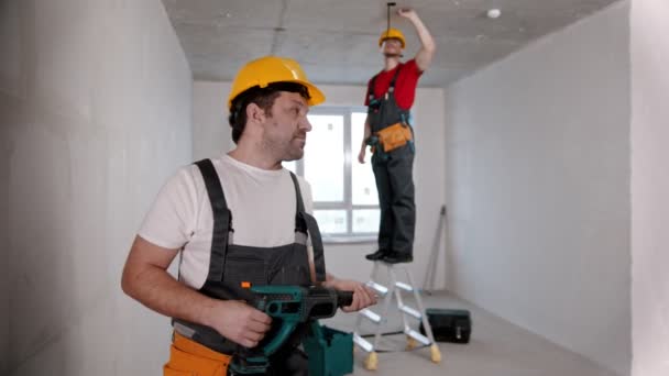 Apartman javítása a piszkozat szobában - egy férfi dolgozó áll a kamera előtt, és adja át fúró egy másik — Stock videók