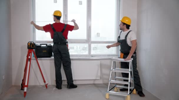 Reparación del apartamento en la habitación: dos trabajadores miden la distancia desde la pared hasta la ventana — Vídeos de Stock