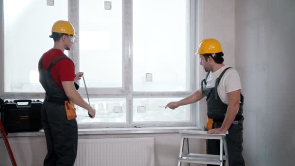 Ремонт квартиры в комнате - двое мужчин, измеряющих площадь с большим окном — стоковое видео