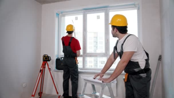 Oprava apartmánu - jeden muž pracovník měření okna v místnosti a další značky výroby na bytovém plánu — Stock video
