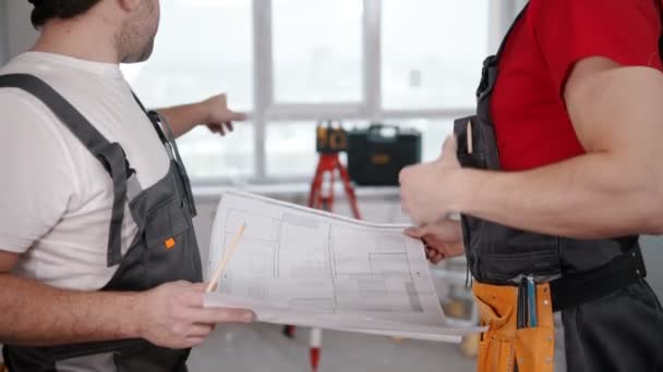 Réparation sur le projet d'appartement - deux travailleurs hommes discutant du plan de l'appartement — Video