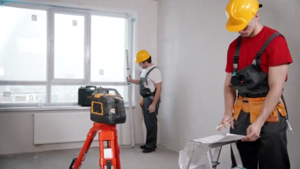Ремонт на черновике квартиры - двое рабочих работают в помещении — стоковое видео