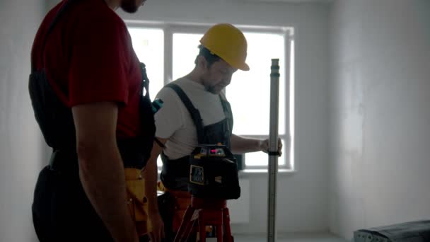 Ремонт на черновике квартиры - двое рабочих, работающих в помещении - лазерная указка и измерительная штука — стоковое видео