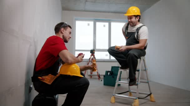 Reparação de apartamento no rascunho de apartamento - homens trabalhadores tendo uma pausa e almoçando no quarto — Vídeo de Stock