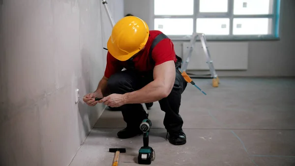 Een man klusjesman werkt met een schroevendraaier in een stopcontact in draft appartement — Stockfoto