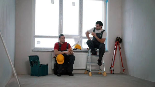Javítás a huzatos lakásban - férfi munkások, akik szünetet és ebédet a szobában — Stock Fotó