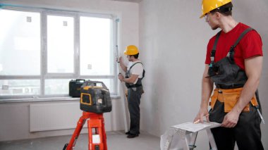 Two men workers measuring the distance from the windowsill to the ceiling and another writing notes about it