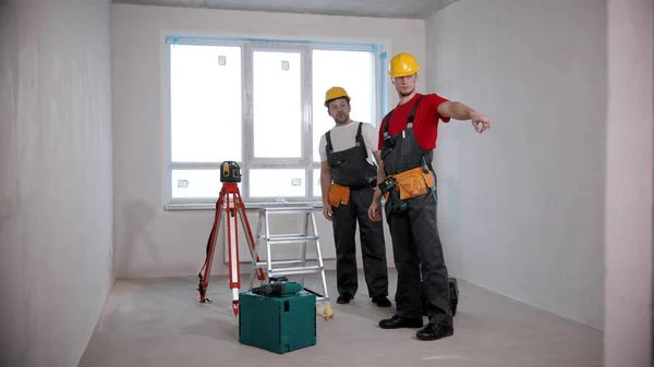 Appartement reparatie - twee mannen arbeiders kijken rond in de ontwerpkamer - een man wijst naar iets — Stockfoto