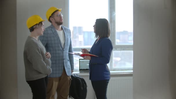 Egy terhes nő a férjével egy ingatlanügynökkel beszél egy új épületben. — Stock videók