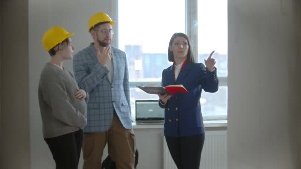 Eine schwangere Frau mit ihrem Mann mit einem Immobilienmakler in einer Wohnung in einem neuen Gebäude - Mann stellt einer Maklerin Fragen — Stockvideo