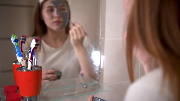 Uma jovem mulher aplicando uma máscara facial em seu rosto — Vídeo de Stock