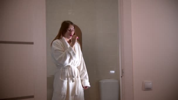 A young woman brushing her teeth at the morning wearing a bathrobe — Stock Video