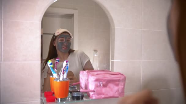 Een jonge vrouw met een masker op haar gezicht dansend en zingend voor de spiegel — Stockvideo
