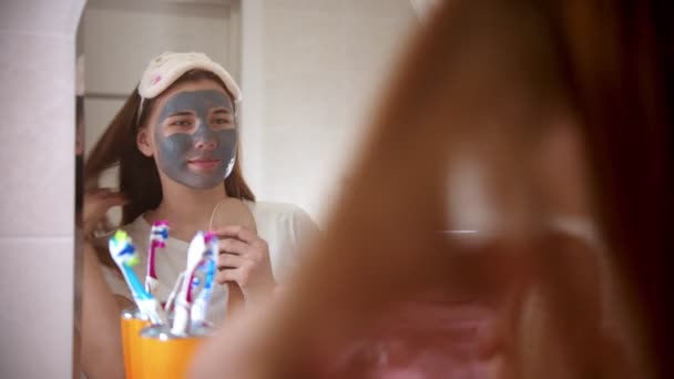 A young attractive woman with a mask on her face dancing and singing in front of the mirror in bathroom — Stock Video