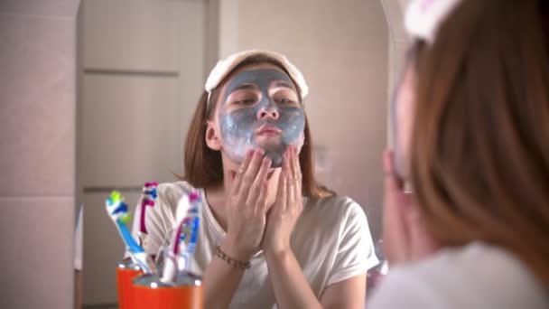 Молодая женщина смывает серую маску с лица — стоковое видео