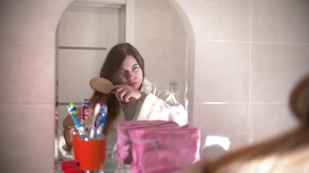 Une jeune femme se brosse les cheveux en regardant dans le miroir — Video