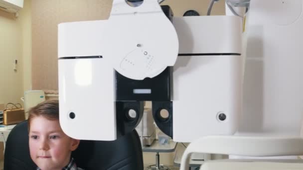 Лікування офтальмолога - маленький хлопчик перевіряє очі з великим пристроєм — стокове відео