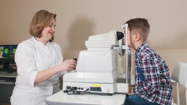 Ophthalmologist treatment - mature smiling woman cheking boys eyes — Stock Video