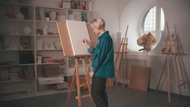 En ung blond kvinna konstnär gör skiss på duken med hjälp av en penna — Stockvideo