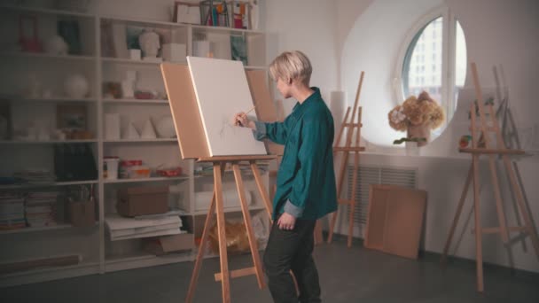 En ung blond kvinna konstnär rita skiss på duken och titta på det — Stockvideo