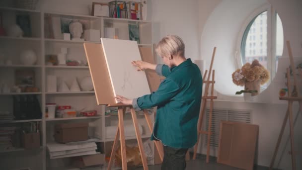 Mladá žena s krátkými vlasy kreslení náčrt na plátně a poslouchat hudbu ve sluchátkách — Stock video