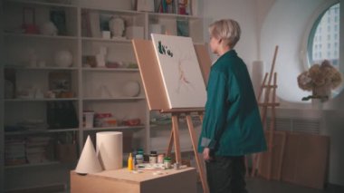 Sanat atölyesinde, ağacın üst dallarını yeşille boyayan genç bir kadın sanatçı paletin rengini alır.