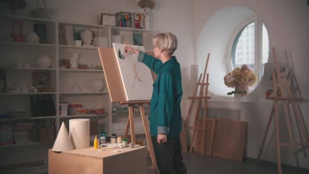En ung kvinna konstnär måla övre grenar av träd i grön färg i konststudio — Stockvideo